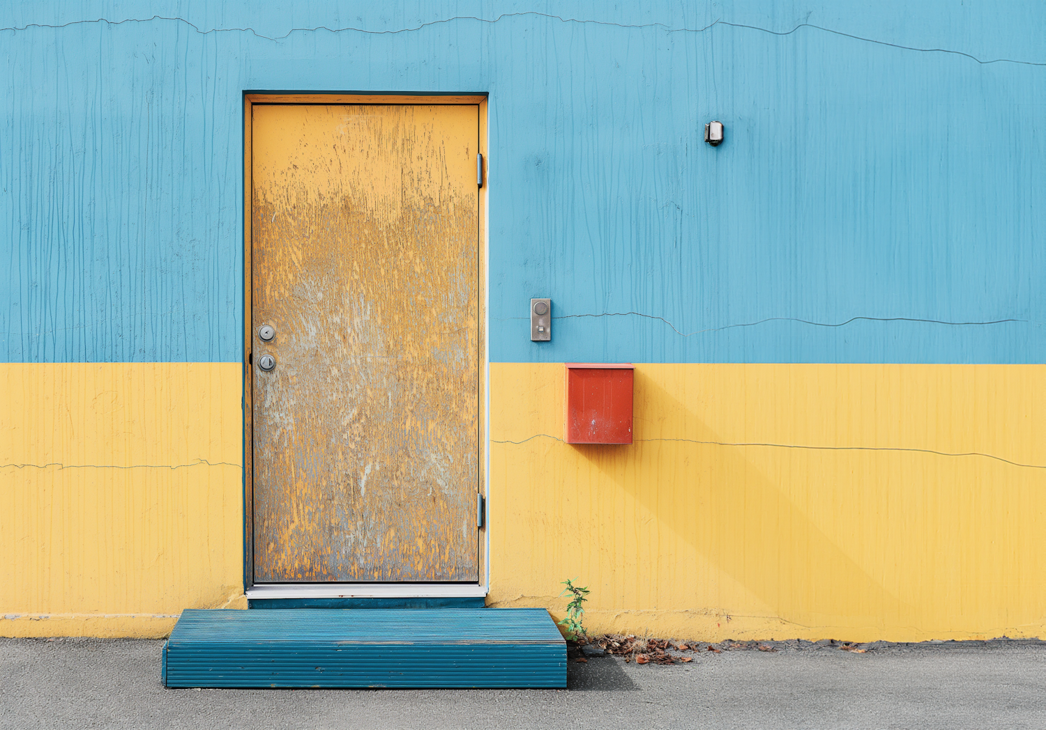 Weathered yellow door set into a painted wall with a red mailbox beside it